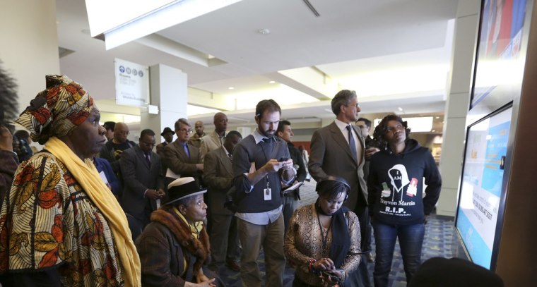 Bystanders and journalists watch the news of an announcement about charges being brought against George Zimmerman at the Washington Convention Center in Washington D.C. April 11, 2012.