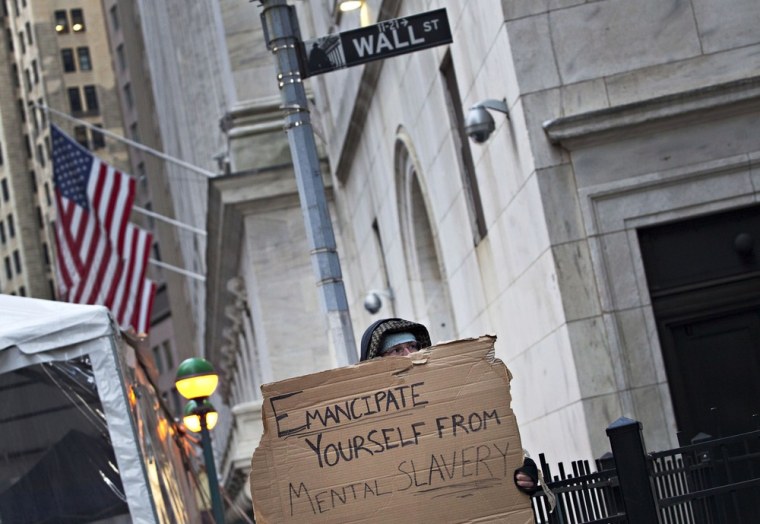 Occupy Wall Street protester Brandon Crozier holds up a sign at the corner of Wall Street and Nassau Street, across the street from the New York Stock Exchange, in the Financial District in New York on April 12.