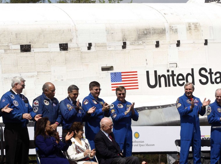 Former U.S. Senator and astronaut John Glenn, seated, is applauded by former shuttle Discovery commanders at the National Air and Space Museum's Steven F. Udvar-Hazy Center at a ceremony for the arrival of space shuttle Discovery (background) in Chantilly, Va. on April 19.