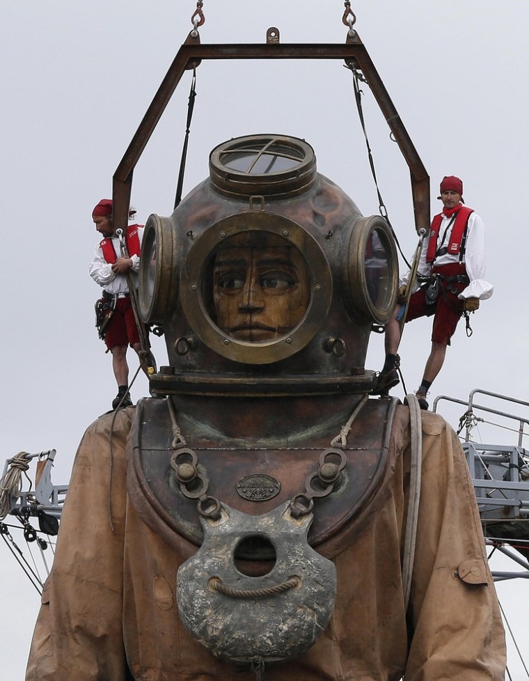 Performers stand on the head of a giant deep sea diver puppet as it is lifted out of the Salthouse Dock in Liverpool, northern England on April 20.