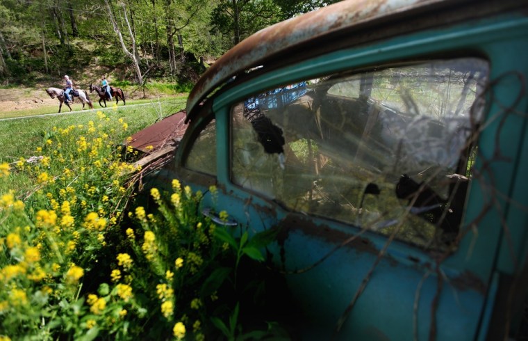 Riders pass an abandoned car during the Owsley County Saddle Club trail ride on April 20 in Booneville, Ky. The trail ride attracts riders from outside the county who contribute much needed revenue.
