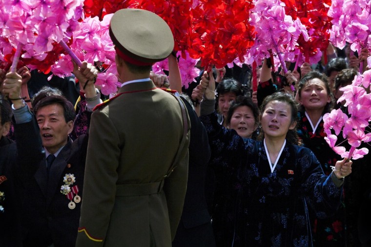 North Korean civilians, some weeping, wave flowers as they look up at Kim Jong Un, unseen, at the end of the military parade on April 15, 2012.