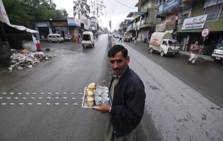 A man carries a tray with cups and pots to sell tea while crossing a road near a market in Abbottabad.