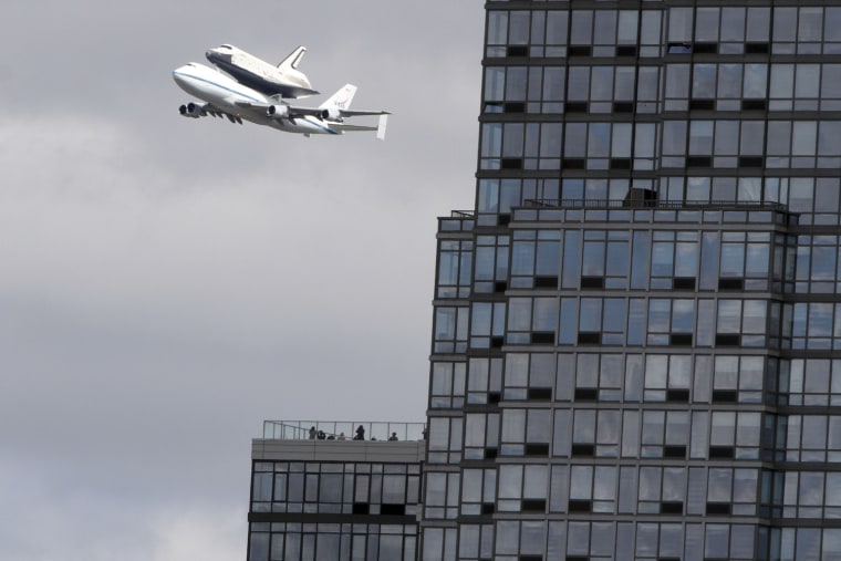 People watch from the balcony of a building as the space shuttle Enterprise, riding on the back of the NASA 747 Shuttle Carrier Aircraft, cruises over the Hudson river, Friday, April 27, 2012 in New York. Enterprise is eventually going to make its new home in New York City at the Intrepid Sea, Air and Space Museum. (AP Photo/Mary Altaffer)
