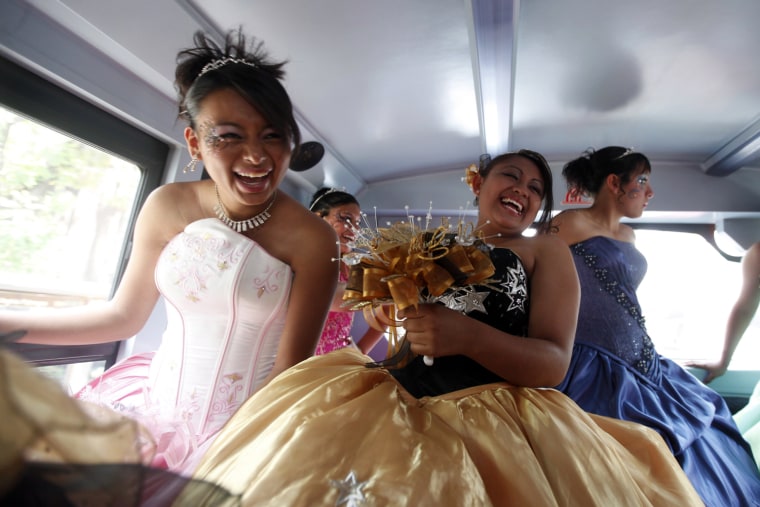 Girls dressed in evening gowns laugh inside a bus.