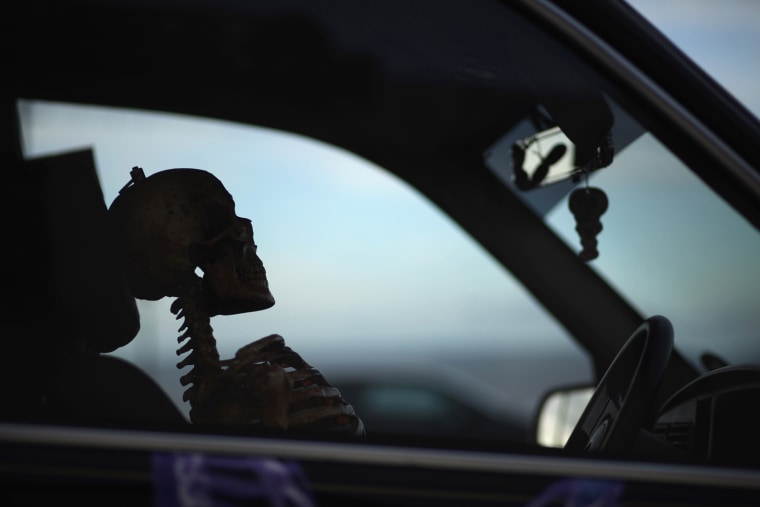 A skeleton sits in the driver's seat of a hearse.