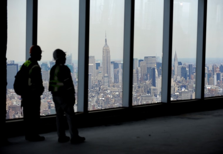 Two construction workers on the 71st floor of One World Trade Center look at a view of the New York skyline, including the Empire State Building.