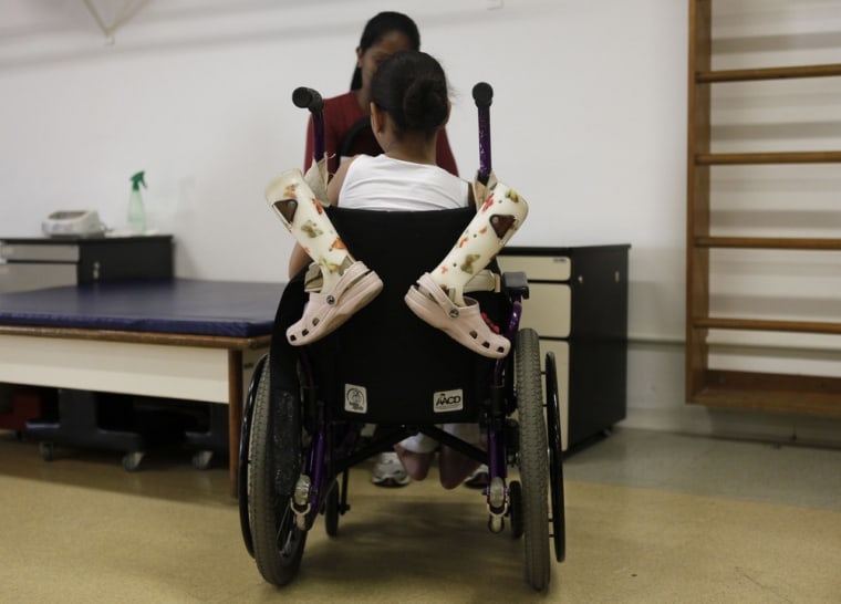 The prosthetic legs of Yara Santos, 9, hang from her wheelchair as she talks with her mother before a session of physical therapy on March 21.