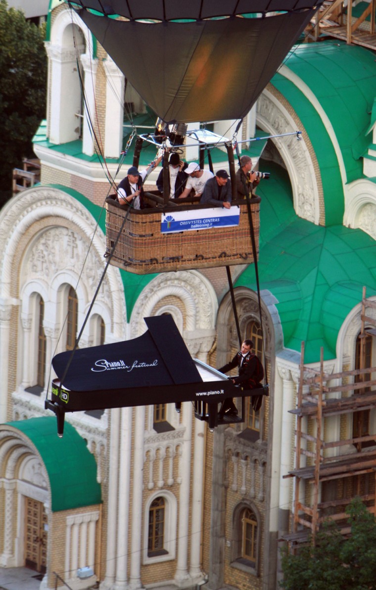 A stuntman pretends to play the piano in the air as he and his cardboard instrument are lifted by a hot air balloon over Vilnius on August 10.