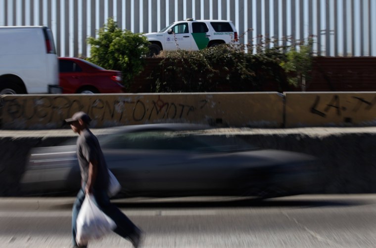 A Border Patrol agent drives his white and green vehicle, above, along the border fence as cars and people cross a road the runs alongside the international border in Tijuana, Mexico, Friday, Former Border Patrol agents Raul Villarreal and his older brother and fellow former agent, Fidel Villarreal, were found guilty of smuggling hundreds of Brazilians and Mexicans to the United States in Border Patrol vehicles.
