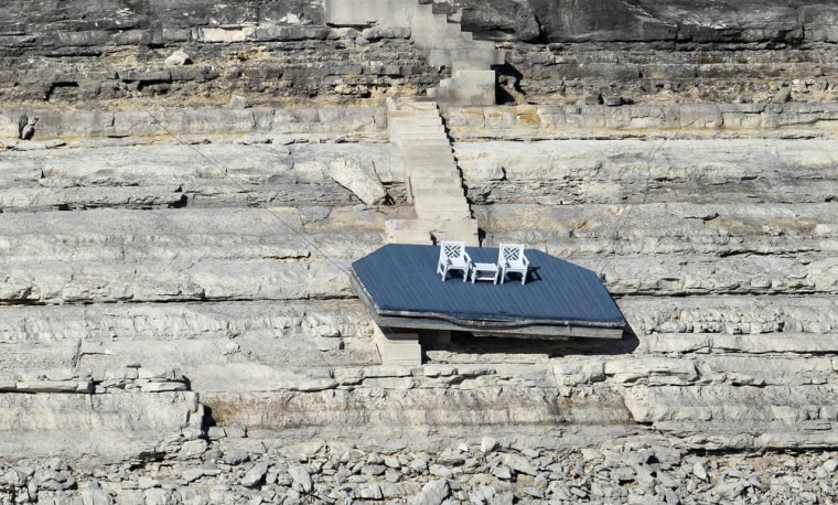 A dock that once floated in Medina Lake hangs by wires on the side of the rocky bank.