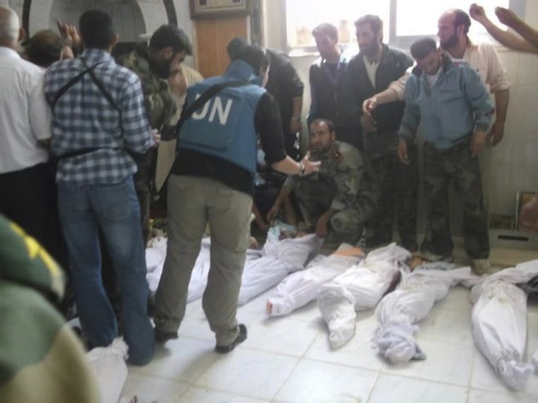 Members of the Syrian Free Army speaks to a person believed to be a member of the United Nations observers mission near the bodies of people allegedly killed by government security forces in Huola in May. A panel appointed by the U.N.'s 47-nation Human Rights Council blamed the government and allied militia for the killing of the more than 100 civilians.
