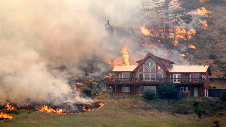 Flames surround a house, Aug. 14, 2012, on a hillside above Bettas Road near Cle Elum, Wash. Wildland firefighters on-site advised that the house survived the fire.