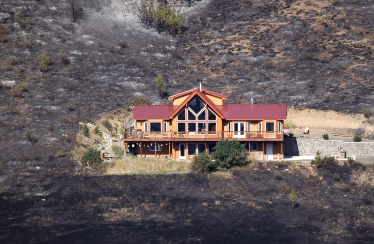 Surrounded by burnt brush and trees, the house shown above still stands, Aug. 15, after surviving a wildfire a day earlier, near Cle Elum, Wash.