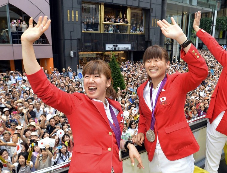 Japan's women's badminton doubles silver medallists Mizuki Fujii, left, and Reika Kakiiwa, wave to the crowds from an open-top bus during a parade for Japan's 2012 London Olympic Games medallists in Tokyo's Ginza shopping district on Aug. 20.