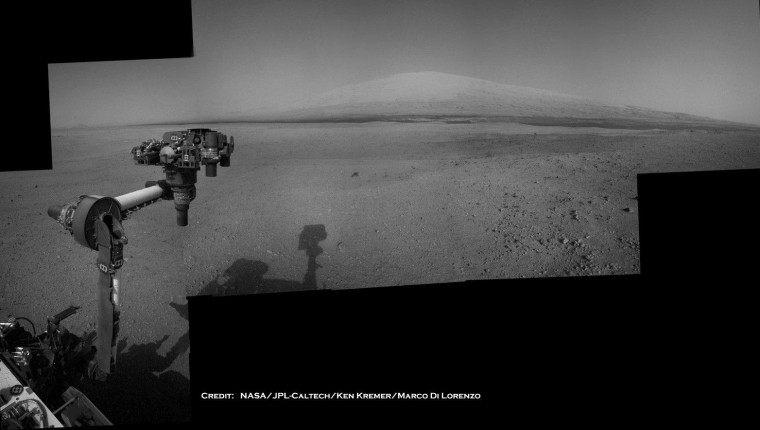 The Mars Curiosity rover's robotic arm takes aim at Mount Sharp in a mosaic that combines navigation-camera imagery from Sols 2, 12 and 14 (Aug. 8, 18 and 20). The shadow of the rover's camera mast is visible in the center foreground, but a significant portion of the mosaic still has to be filled in.