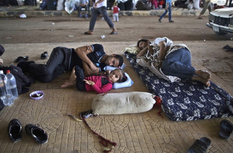 A Syrian girl lies on the ground next to her father, while they take refuge at a Turkey border crossing.