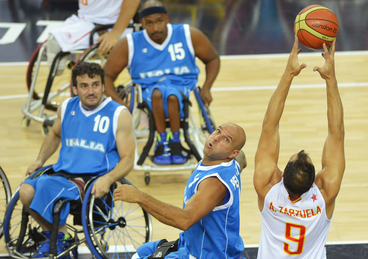 Members of the Italian team look on as Spain's Alejandro Zarzuela Beltran, right, attempts a shot during their preliminary men's group A wheelchair basketball match, Aug. 30.