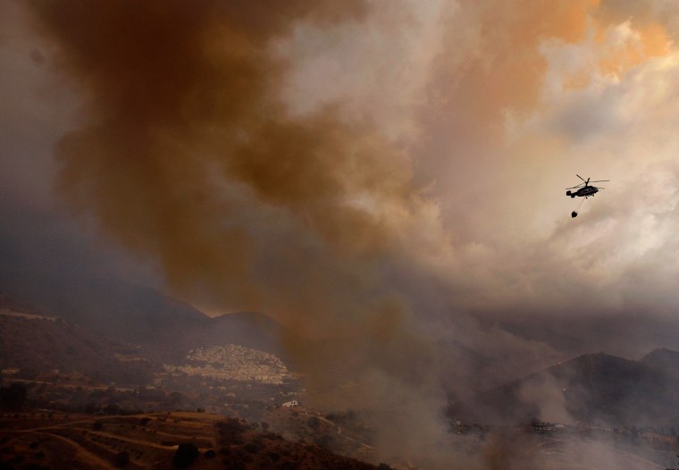 A firefighting helicopter transporting a water bucket heads towards a fire in Ojen, southern Spain, on Aug. 31. Spanish officials say some 4,000 people have been evacuated from their houses as a wildfire abetted by strong winds spread rapidly through hills around the popular southern tourist city of Marbella.