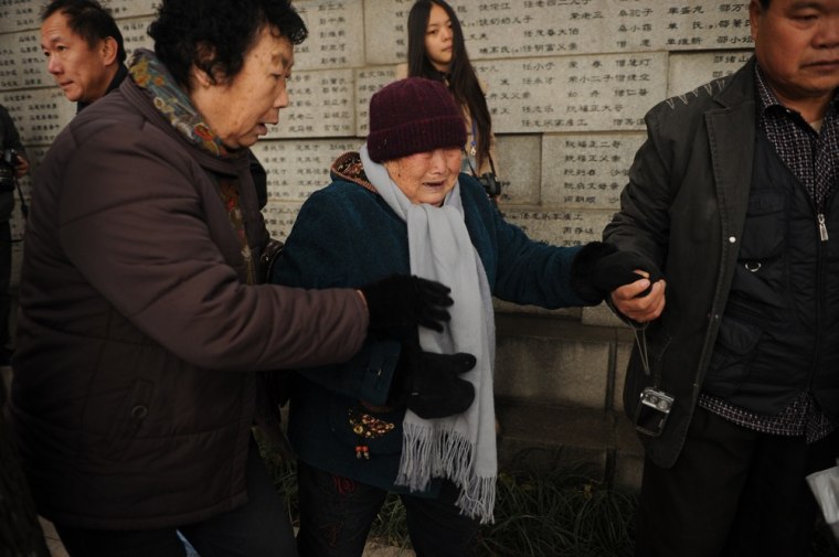 A Nanjing massacre survivor, center, cries after placing flowers on a wall with the names of victims at the Memorial Museum in Nanjing on December 13, 2012.