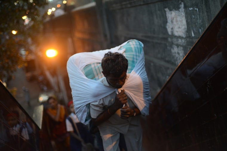 A worker carries a load of clean clothes to be delivered after being washed and ironed as he leaves the Dhobi Ghat in Mumbai.