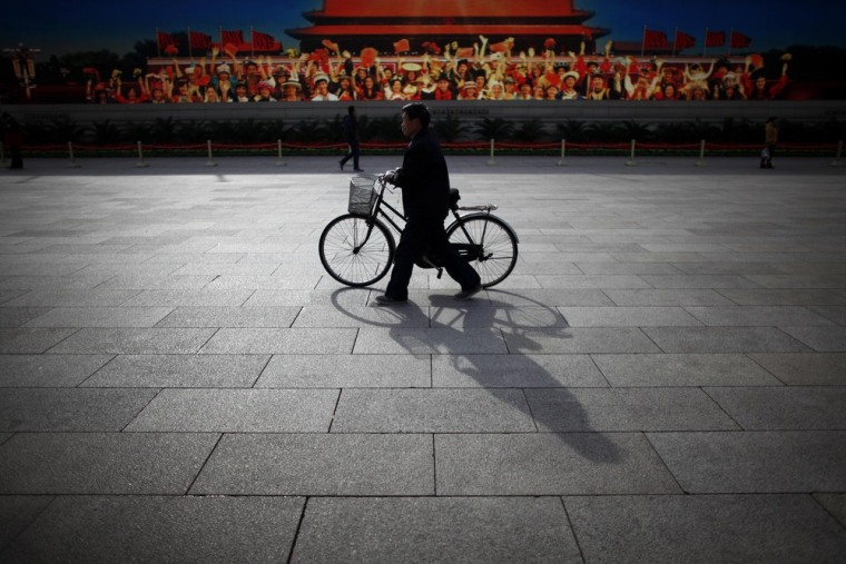 A man walks with his bicycle in front of a screen showing propaganda displays near the Great Hall of the People at Beijing's Tiananmen Square in this ...