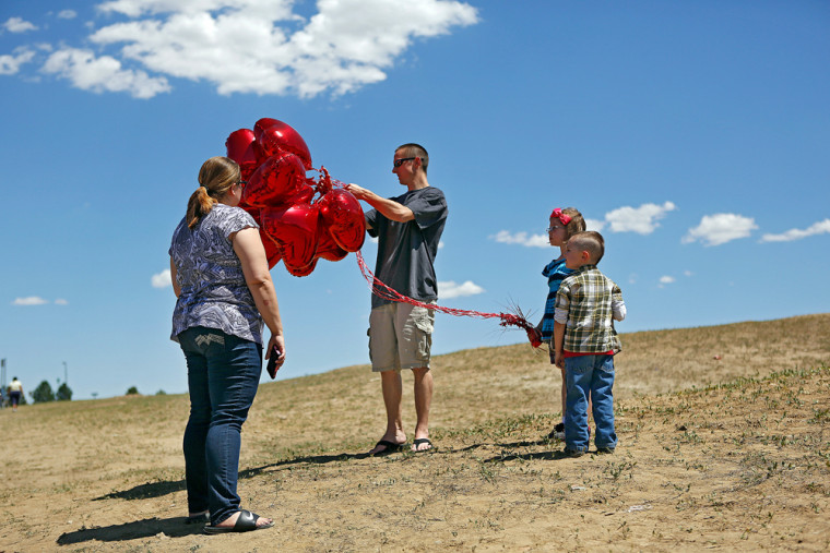Eric and Sophia Gettys of Aurora, Colo. help their children Gabriel, 4, and Gabriela, 6, with 12 heart-shaped balloons that they placed at a makeshift memorial near the Century 16 Movie Theaters at the Aurora Town Center on Saturday. The family had planned to go to a movie at another theater to get their minds off the tragedy but found it closed because one of the shooting victims had worked there so they saw it as a sign to visit the memorial and leave one balloon for each victim.
