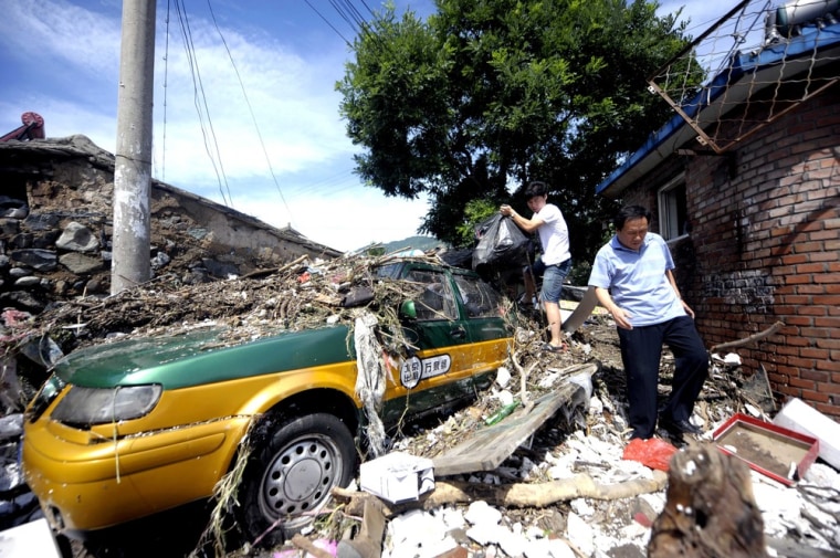 Residents try to get through a residential alley which is blocked by a taxi which was washed there after a storm hit the city, blowing off rooftops which killed two people and injured six others, in Beijing on July 22, 2012 .
