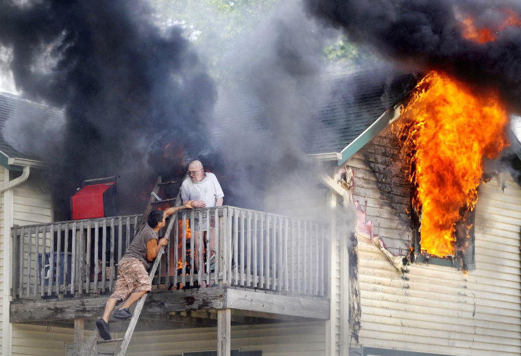 Edwardo Martinez tries to coax Pete Lui off the balcony as flames spread through the second floor apartment of his home in Racine, Wis. on July 24, 2012.