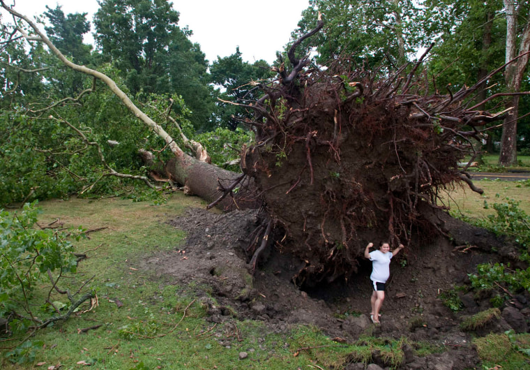 Jessica Stansfield poses for a photo below an enormous uprooted tree after the town was hit by a tornado in Elmira, N.Y., July 26. Severe thunderstorms unleashed heavy rain and strong winds across parts of the Midwest and Northeast on Thursday, grounding hundreds of flights and leaving tens of thousands of people without power.