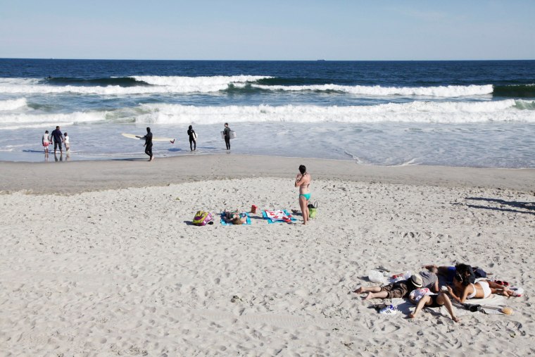 Sunbathers and surfers walk on Rockaway Beach in the Queens neighborhood of New York in May.