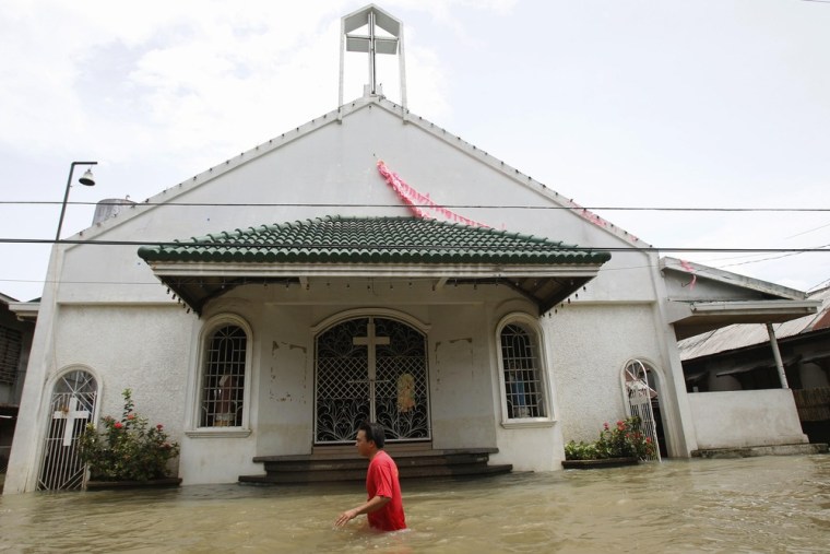 A resident wades through waist-deep floodwaters brought by tropical storm Saola as he passes by a Catholic church at Almacen town in Bataan province, north of Manila on July 31, 2012.