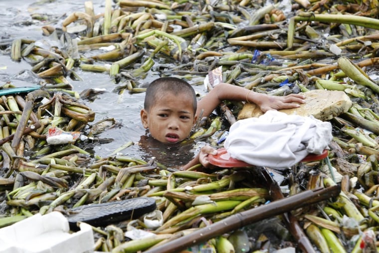 A boy holds his shirt on the lid of a plastic container to keep it dry while gathering recyclable materials from the debris swept by strong winds in Manila bay on July 31, 2012.