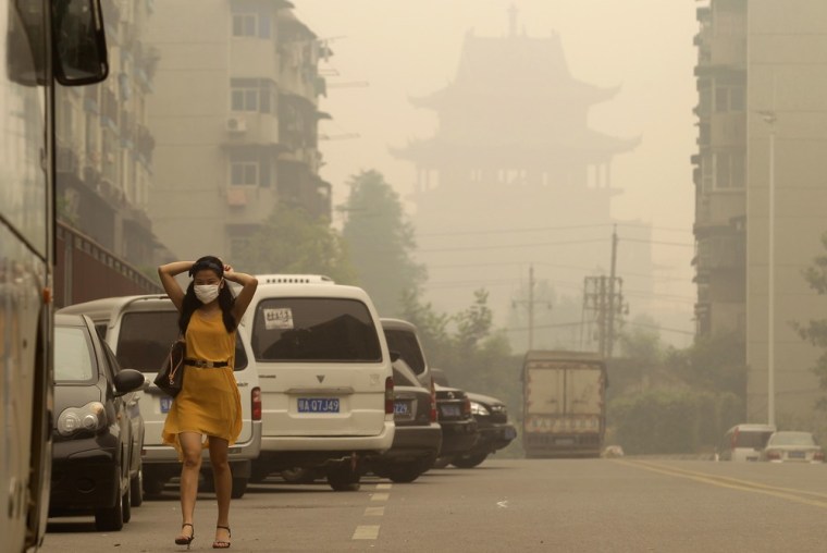 A woman wears a mask as she walks along a street in front of a Chinese temple during a hazy day in Wuhan, Hubei province on Monday. China's carbon emissions could be nearly 20 percent higher than previously thought, a new analysis of official Chinese data showed on Sunday, suggesting the pace of global climate change could be even faster than currently predicted.