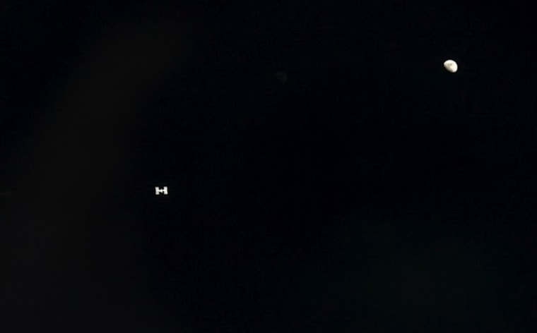 The International Space Station looks like little more than a speck with solar panels in this picture, which was taken from the shuttle Atlantis during its approach on July 10. A first-quarter moon shines on the right side of the frame.