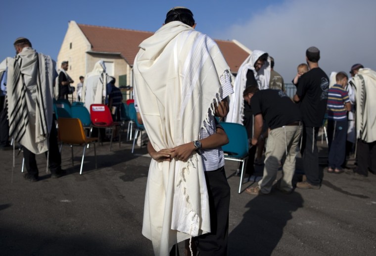 Israeli settlers wrapped in a tallit, or prayer shawl, is hugged by a child as he prays in front of houses in the Ulpana neighborhood of Beit El settlement.