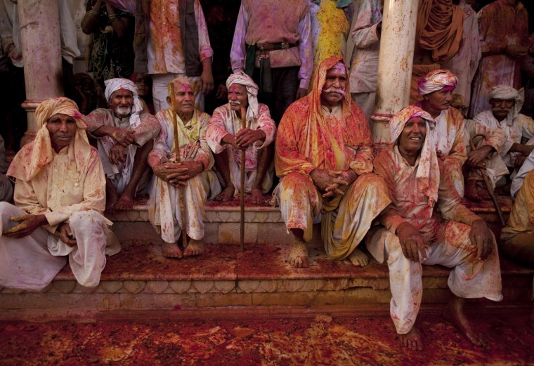 Indian Hindu men watch during Lathmar Holi at Nandagram Temple, in Nandgaon,India, Saturday, March 3, 2012. According to tradition which has its roots in Hindu mythology men from Barsana arrive at the temple where they are soaked in colored water by men from Nandgaon, believed to be Lord Krishna's village, and then beaten by the women of the village with wooden sticks as they depart the town. (AP Photo/Kevin Frayer)
