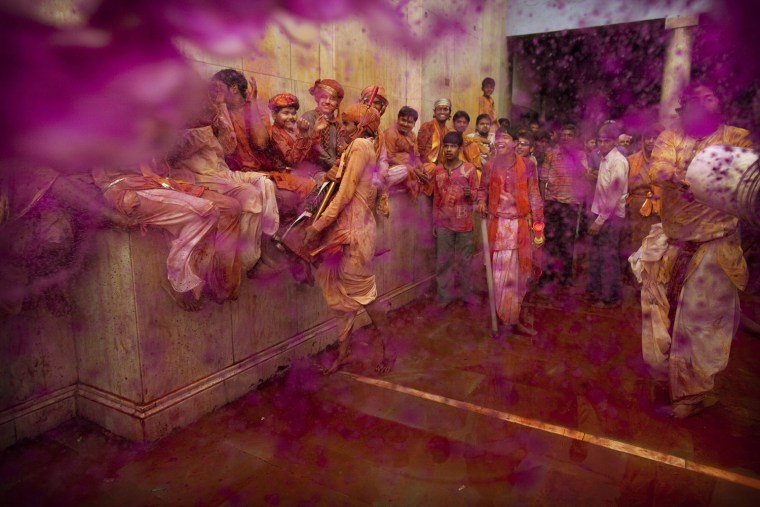 An Indian Hindu worshipper throws a bucket of colored water on others during Lathmar Holi at Nandagram Temple, in Nandgaon, India, Saturday, March 3, 2012. According to tradition which has its roots in Hindu mythology men from Barsana arrive at the temple where they are soaked in colored water by men from Nandgaon, believed to be Lord Krishna's village, and then beaten by the women of the village with wooden sticks as they depart the town. (AP Photo/Kevin Frayer)