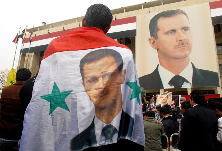 A Syrian man wears as a cape his national flag with a portrait of President Bashar al-Assad during a rally in support of their leader and the army in Damascus on February 14, 2012. AFP PHOTO/PATRICK BAZ (Photo credit should read PATRICK BAZ/AFP/Getty Images)