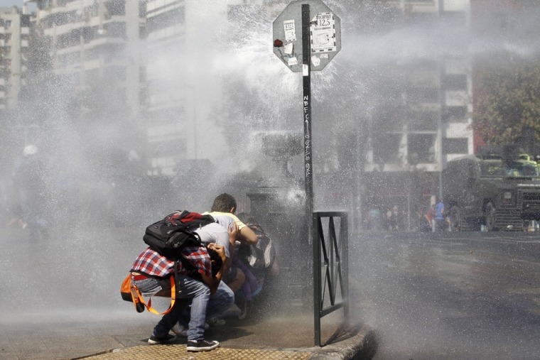 Student protesters take cover from a jet of water released form a riot police vehicle during a demonstration against the government demanding changes in the public state education system, in Santiago March 15, 2012. March 15, 2012. Chilean students have been protesting against what they say is profiteering in the state education system. REUTERS/Ivan Alvarado (CHILE - Tags: POLITICS CIVIL UNREST EDUCATION)