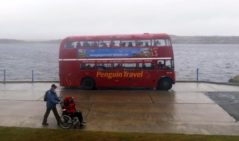A woman shoots a video of a double-decker bus from her wheelchair in Port Stanley on Thursday.