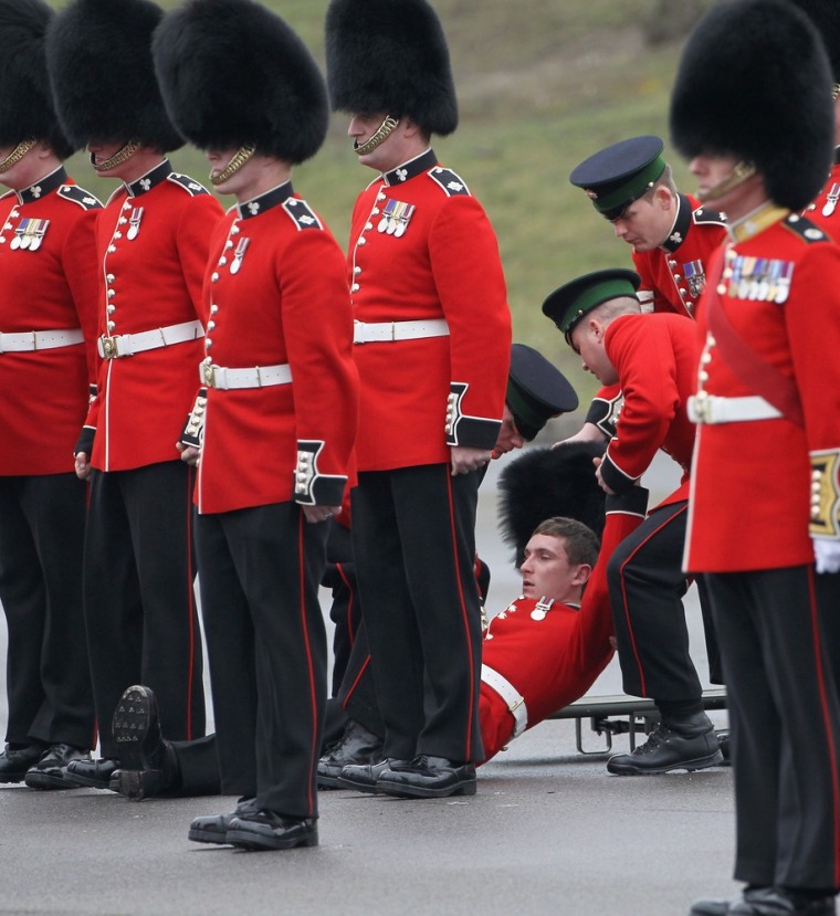 ALDERSHOT, ENGLAND - MARCH 17: A soldier is helped to his feet after fainting as Catherine, Duchess of Cambridge takes part in a St Patrick's Day parade as she visits Aldershot Barracks on St Patrick's Day on March 17, 2012 in Aldershot, England. The Duchess presented shamrocks to the Irish Guards at a St Patrick's Day parade during her visit. (Photo by Chris Jackson/Getty Images)