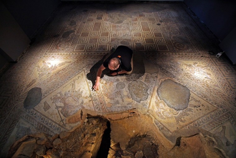 CIRENCESTER, UNITED KINGDOM - MARCH 19: David Rawcliffe, house and monument steward at the National Trust's Chedworth Roman Villa cleans a Roman mosiac in the new environmentally-controlled conservation shelter on March 19, 2012 near Cirencester, England. Opened this month, the multi-million pound building allows visitors to walk on suspended walkways just above the 1600-year-old Roman floors and to see recently excavated mosaics not seen for 150 years, with more to be uncovered over the coming year. (Photo by Matt Cardy/Getty Images)