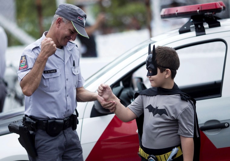 A police officer jokes with a boy dressed as Batman, during a visit to a school by retired Brazilian police officer Andre Luiz Pinheiro, 50, who dresses up as Batman, in Taubate city in Sao Paulo state March 17, 2012. Pinheiro has been called to help police patrol the crime-ridden streets of Taubate, in Brazil. He was officially presented in the districts with the highest crime rates in Sao Paulo state. Police captain Warley Takeo, one of the policemen who decided to bring in the character to help them fight drug traffickers, said the measure would bring long-term benefits. Takeo said making a connection between the police and Batman would help children have a clearer idea of good and bad. Picture taken March 17. REUTERS/Roosevelt Cassio (BRAZIL - Tags: CRIME LAW CIVIL UNREST ENTERTAINMENT SOCIETY)