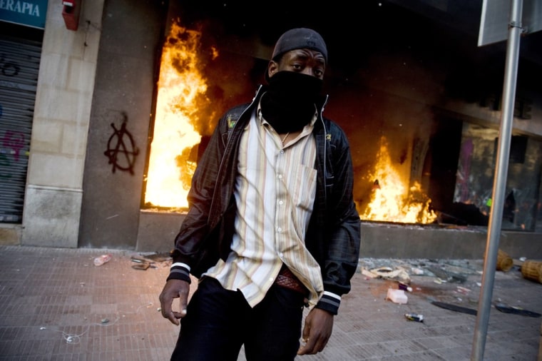 A masked demonstrator walks past a burning Starbucks during heavy clashes with riot police during a 24-hour strike on March 29 in Barcelona.