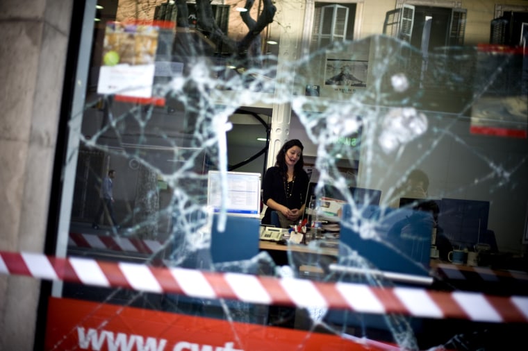 A Carslon Wagonlit Traves employee is seen through a broken window on March 30, in Barcelona, Spain. Violent clashes between demonstrators and riot police in the past 24 hours has left scores injured and led to 74 people being detained.