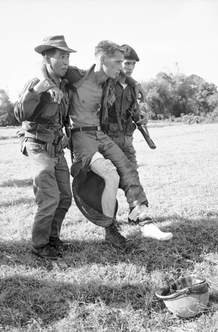 An American sergeant of the 1st infantry division winces in pain as two Vietnamese soldiers drag him to an evacuation helicopter. He was wounded by grenade-shrapnel in both legs and chest when a booby-trapped grenade exploded in front of him as he searched a house on an operation north of the new 1st Div. Headquarters at Phul Loi, 17 miles north of Saigon on Nov. 12, 1965.