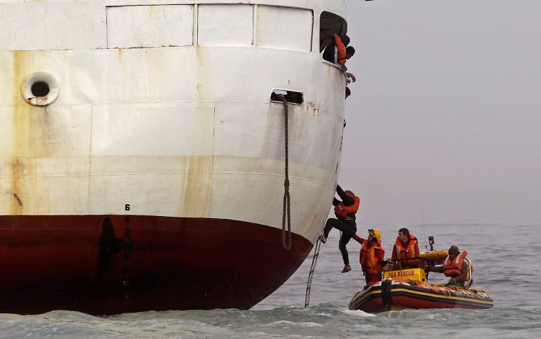 Rescue workers help a crew member from a stranded trawler into a rescue boat.