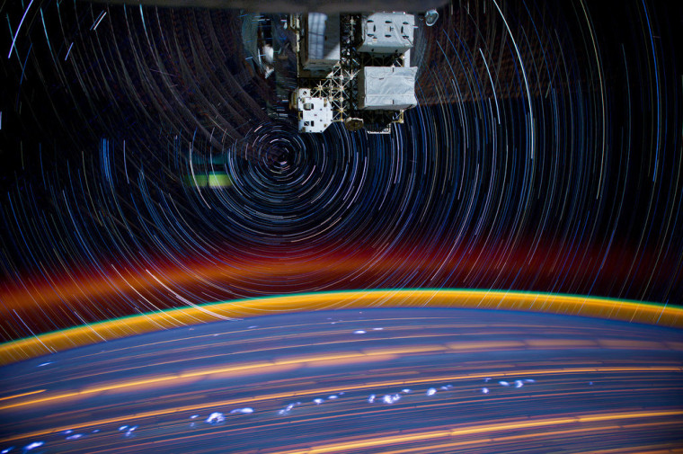 This is a composite of 18 time-exposure images photographed from a mounted camera on the International Space Station, from approximately 240 miles above Earth. The image is filled with star trails and spiraling reflections from the space station's solar arrays.