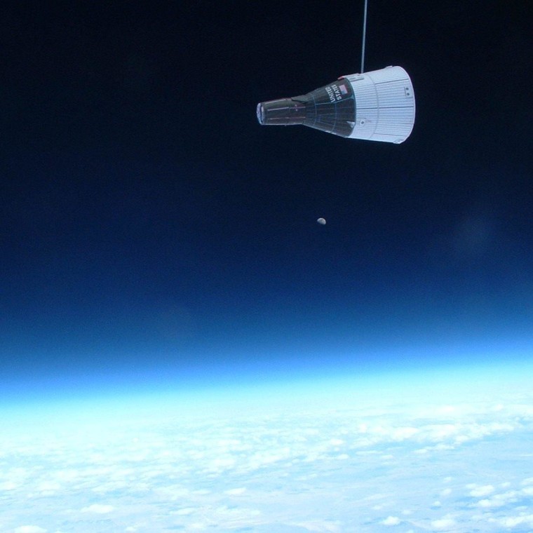 A 2-inch-long paper model of a 1960s-era Gemini capsule hangs from a string in front of a camera mounted on a balloon-borne platform at an altitude of more than 97,000 feet. Meanwhile, the moon hangs in the far background, sans string.